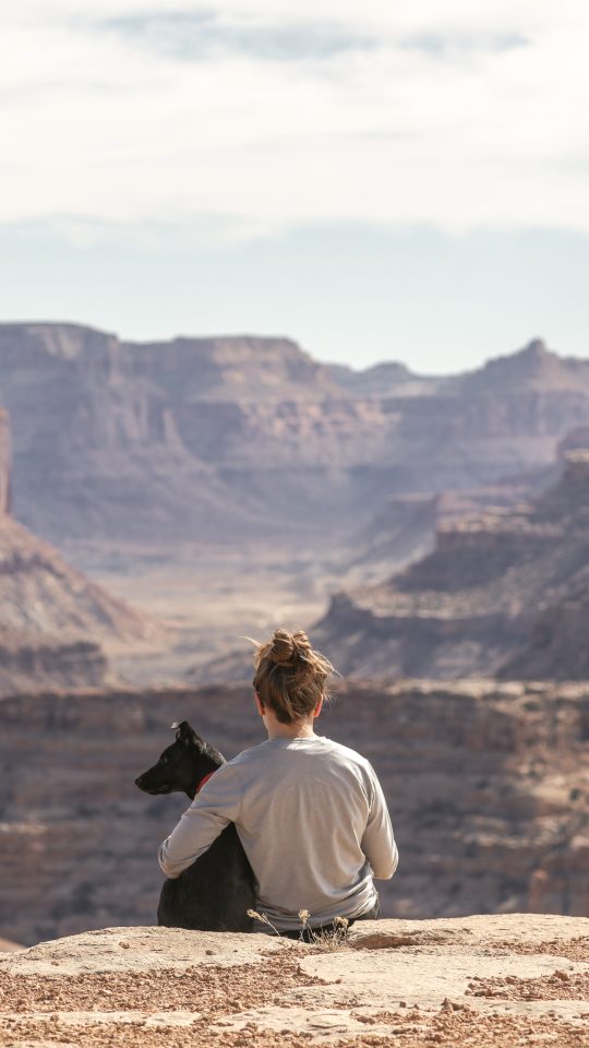 person with dog sitting on Grand Canyon cliff